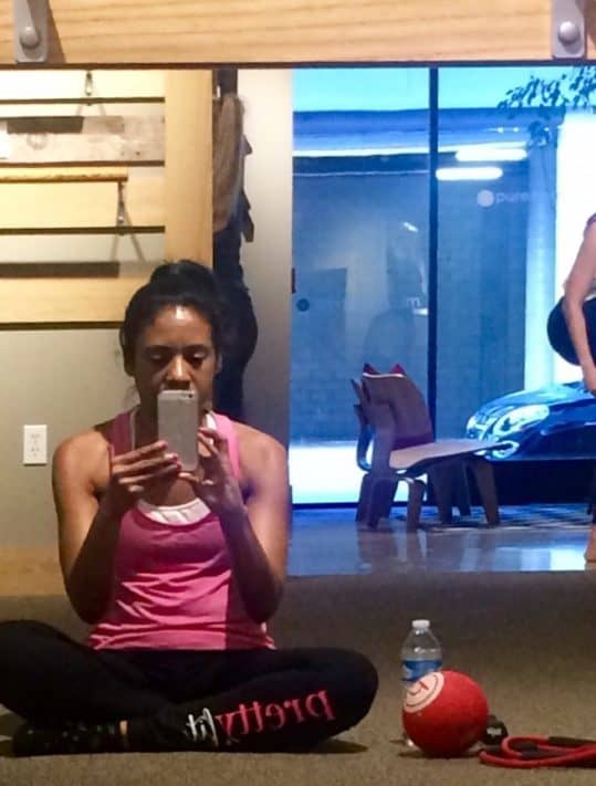sitting cross-legged in the barre studio in black leggings and a pink tank top