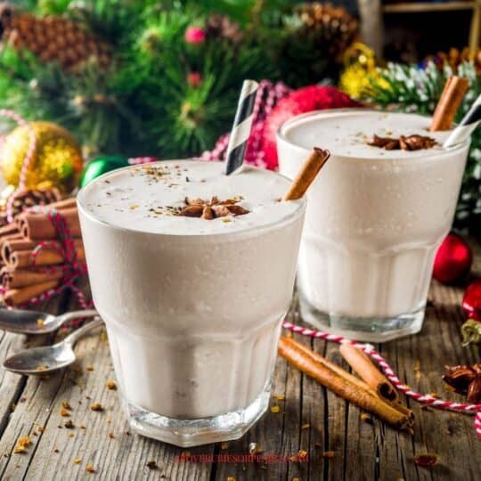 2 glasses of eggnog with straws and cinnamon sticks in front of the Christmas tree