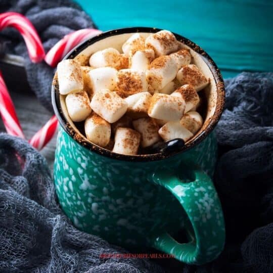 a mug of hot chocolate topped with marshmallows next to 2 candy canes forming a heart