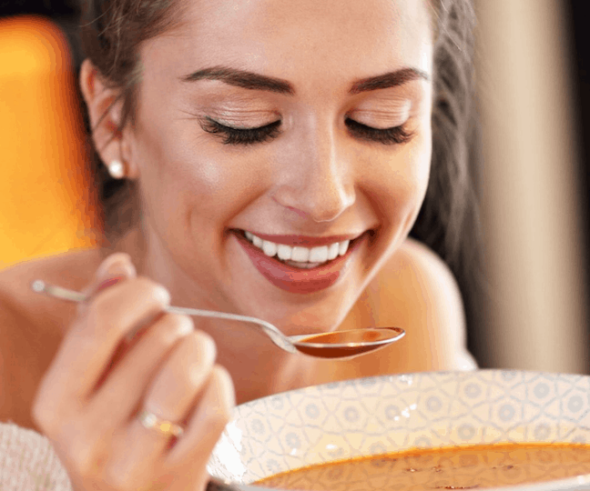smiling lady eating a bowl of soup
