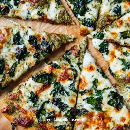 A pizza topped with cheese, kale, and pesto is sliced into 8 wedges