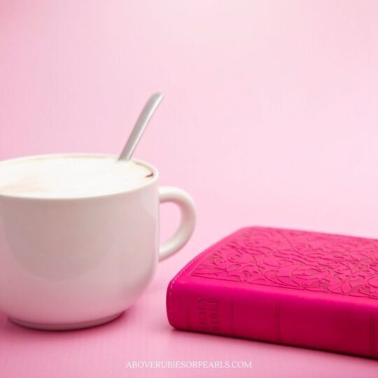 a pink Bible is next to a frothy hot beverage on a pink counter