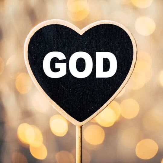 God is written on a heart-shaped sign with sparkling lights in the background