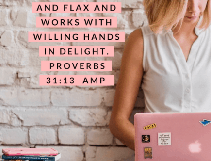 A Proverbs 31 Business Woman is working on her pink laptop. She is sitting on a hardwood floor, leaning against a white brick wall. She has a stack of books and other resources next to her, including a girl boss book.