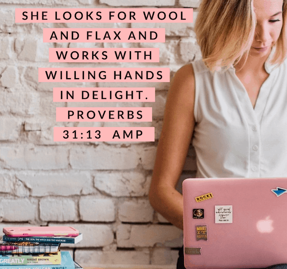 A Proverbs 31 Business Woman is working on her pink laptop. She is sitting on a hardwood floor, leaning against a white brick wall. She has a stack of books and other resources next to her, including a girl boss book.