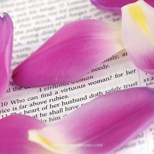 A Bible is open to a scripture describing the Proverbs 31 Woman. Orchid flower petals are scattered on top.