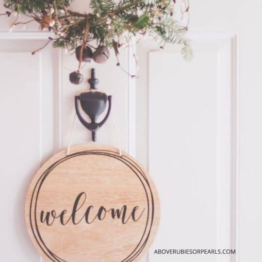 A welcome sign is hanging on a white door beneath a wreath.