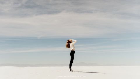 A lady standing on the beach is looking up but covering her eyes