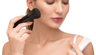 Lady in white dress applying blush to cheek with makeup brush