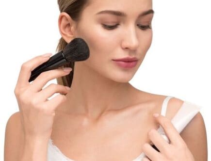 Lady in white dress applying blush to cheek with makeup brush