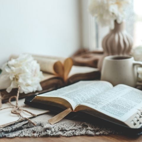 Open Bible with flowers and coffee on a wooden table in a peaceful devotional setting near a window