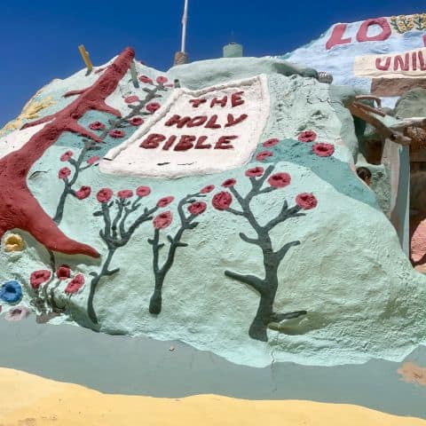 Close-up of Salvation Mountain showing “The Holy Bible” painted among colorful flowers with the cross visible above.