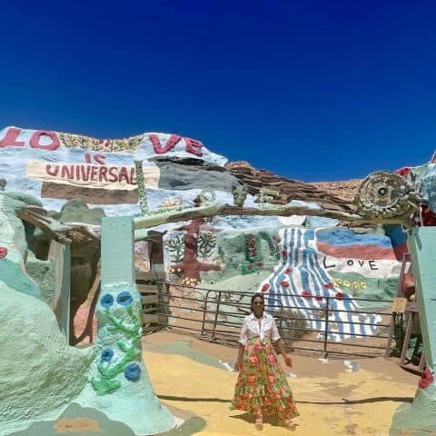 Woman walking in front of Salvation Mountain with “Love Is Universal” painted on the colorful desert art installation.