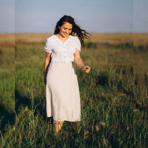 Smiling woman walking peacefully through a field, looking downward, representing quiet confidence in Christ and freedom from striving.