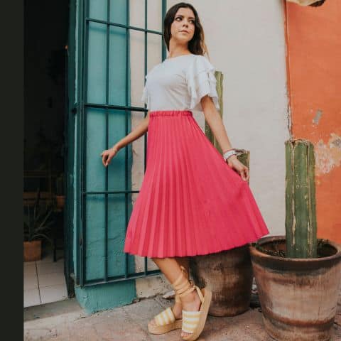Woman wearing modest spring outfit: pink pleated midi skirt with white ruffled sleeve tee and platform wedges