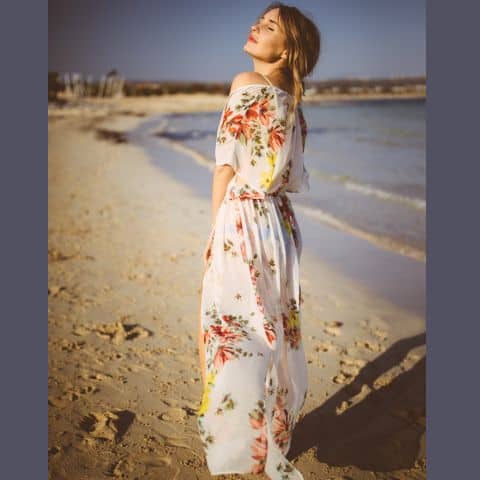 Woman in modest spring outfit wearing floral beach coverup over swimsuit on sunny shore
