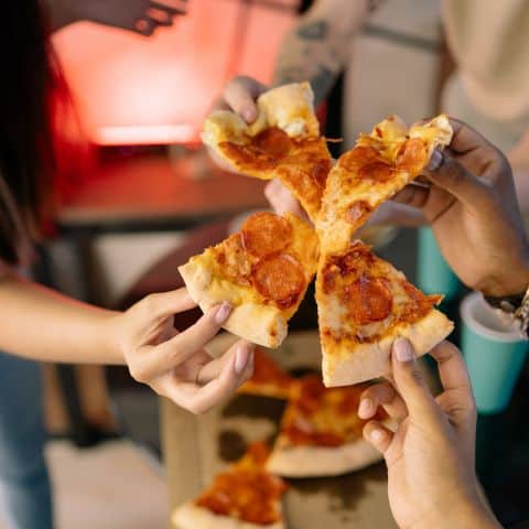 Four friends gathered around a table sharing pizza and laughing together, showing connection and a sense of belonging.