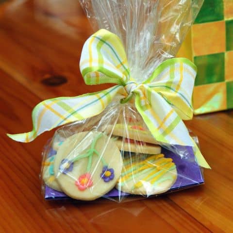 Clear cellophane bag of decorated Easter cookies tied with a pastel plaid bow, reflecting thoughtful and generous hospitality.